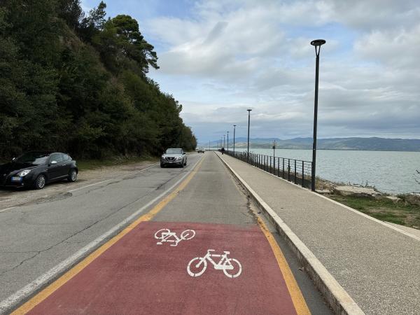 Tratto ciclovia in sede stradale, di colore rosso. Macchine in carreggiata contraria, e marciapiede rialzato a destra